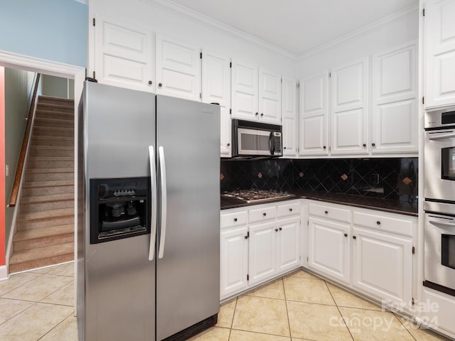 kitchen featuring white cabinetry, stainless steel appliances, tasteful backsplash, light tile patterned floors, and ornamental molding