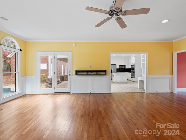 unfurnished living room with ceiling fan, ornamental molding, and light wood-type flooring