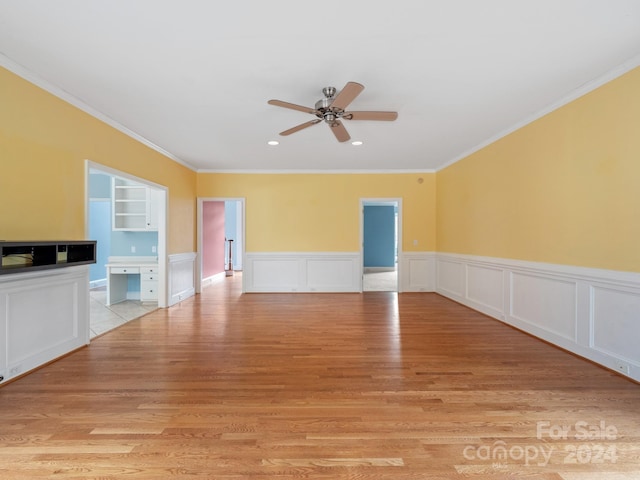 unfurnished living room with built in desk, light hardwood / wood-style floors, ceiling fan, and ornamental molding