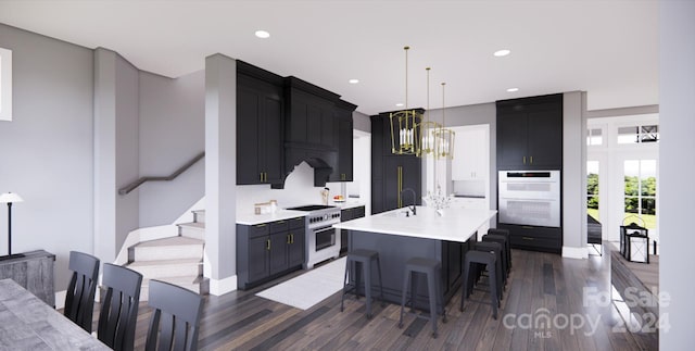 kitchen with dark wood-type flooring, hanging light fixtures, a breakfast bar area, an island with sink, and white appliances