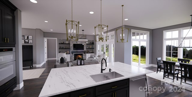 kitchen featuring hanging light fixtures, sink, an island with sink, dark hardwood / wood-style floors, and a fireplace