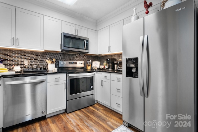 kitchen with stainless steel appliances, dark wood-type flooring, tasteful backsplash, ornamental molding, and white cabinetry