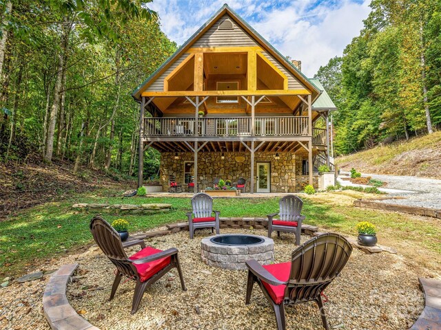 rear view of property featuring stone siding, a wooden deck, a fire pit, and a patio