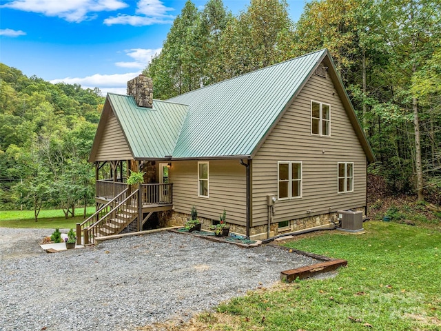 chalet / cabin featuring central AC unit, a chimney, stairway, metal roof, and a front lawn