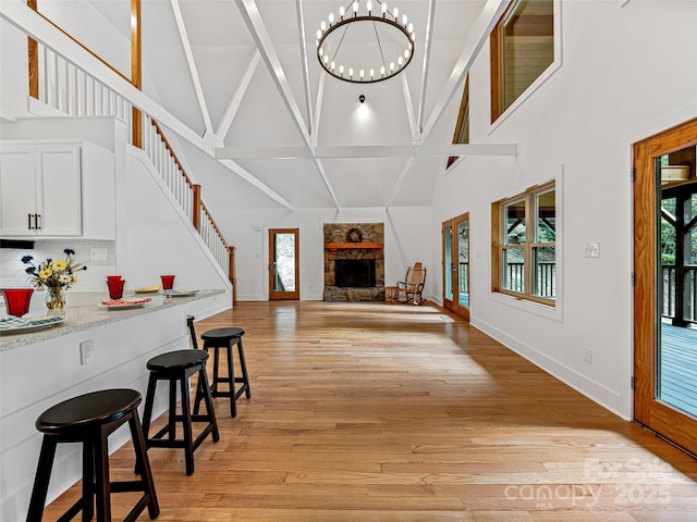 living area with light wood finished floors, plenty of natural light, a chandelier, and a stone fireplace