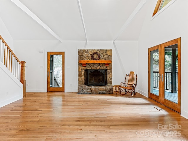 unfurnished living room with french doors, light wood-style flooring, a stone fireplace, baseboards, and stairs