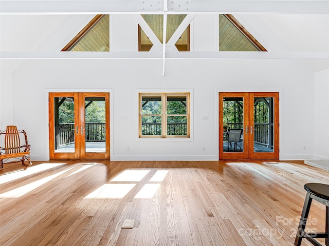 unfurnished living room featuring high vaulted ceiling, baseboards, hardwood / wood-style floors, and french doors