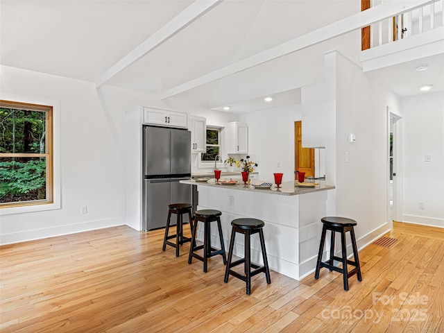 kitchen with light wood finished floors, a breakfast bar area, freestanding refrigerator, white cabinets, and baseboards