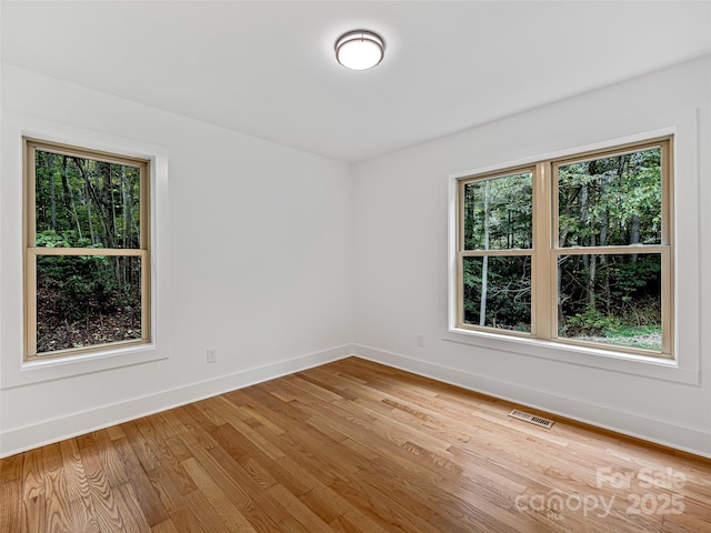 spare room featuring a wealth of natural light, light wood-style flooring, visible vents, and baseboards