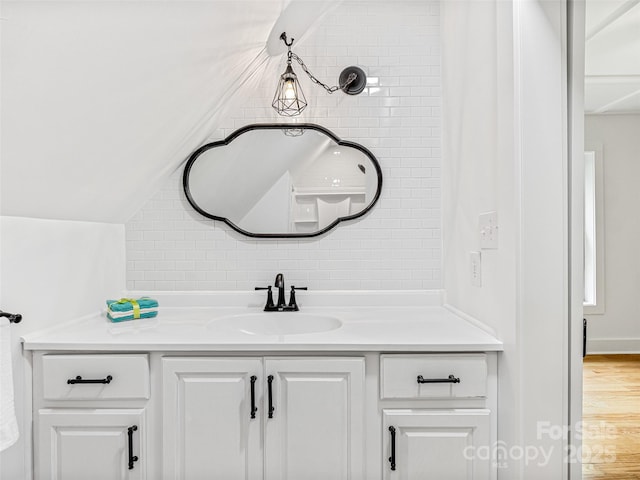 bathroom with vaulted ceiling, wood finished floors, vanity, and decorative backsplash