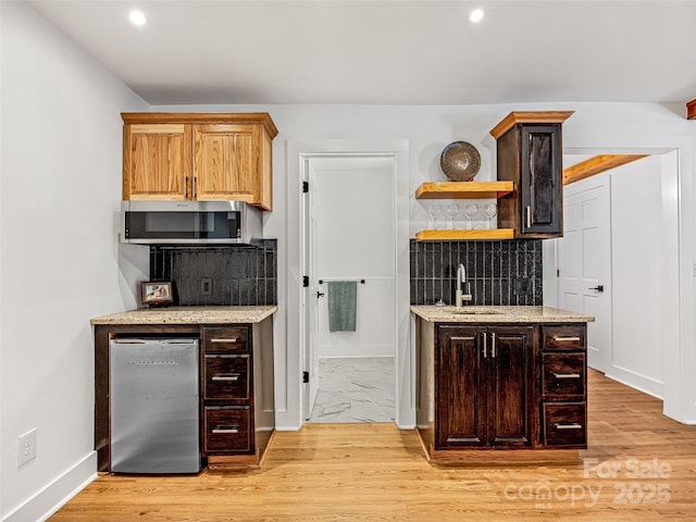 kitchen featuring refrigerator, stainless steel microwave, a sink, and light stone countertops