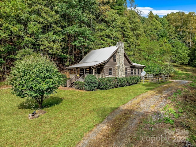 view of side of property featuring a chimney, dirt driveway, a porch, a lawn, and log exterior