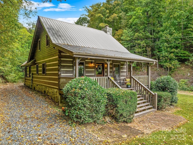 view of front facade featuring covered porch, a chimney, and metal roof