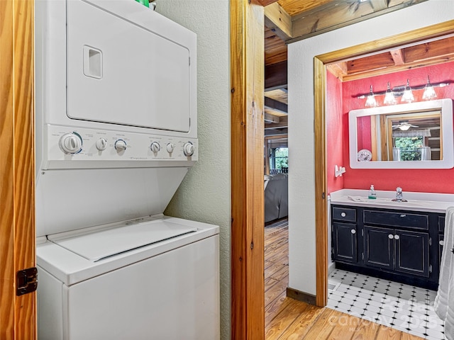 clothes washing area featuring stacked washer and dryer, a textured wall, light wood-style floors, laundry area, and plenty of natural light