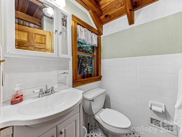 bathroom with tile walls, visible vents, a textured wall, toilet, and vanity