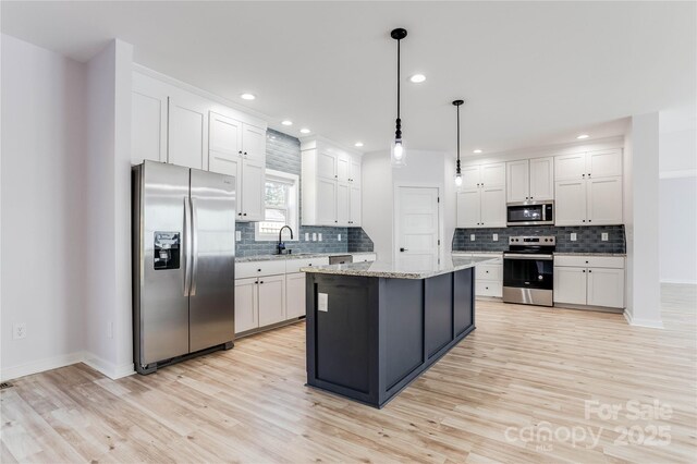 kitchen with pendant lighting, stainless steel appliances, a center island, light stone countertops, and white cabinets