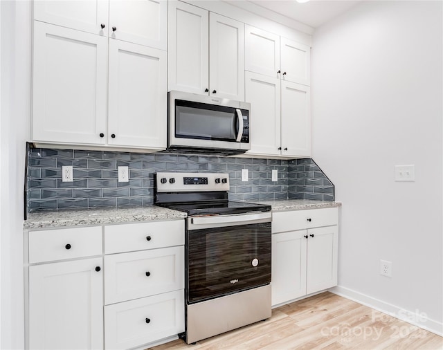 kitchen with appliances with stainless steel finishes, white cabinetry, backsplash, light stone countertops, and light hardwood / wood-style flooring