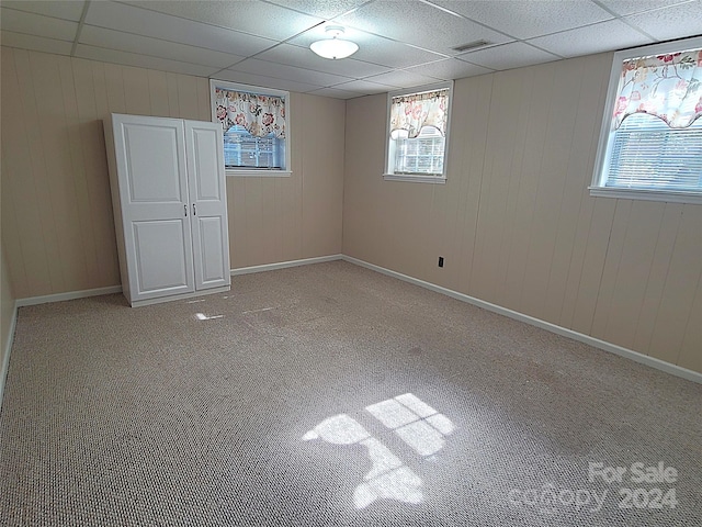 spare room featuring light colored carpet, a paneled ceiling, and wooden walls