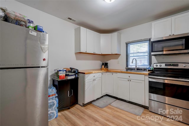 kitchen featuring white cabinets, sink, stainless steel appliances, light wood-type flooring, and butcher block countertops