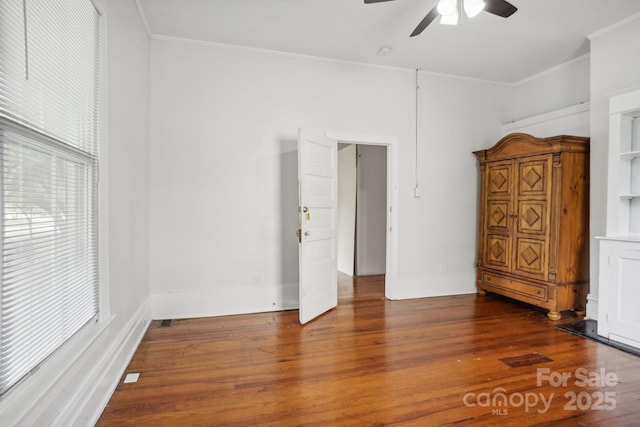 empty room with ornamental molding, dark wood-type flooring, and ceiling fan