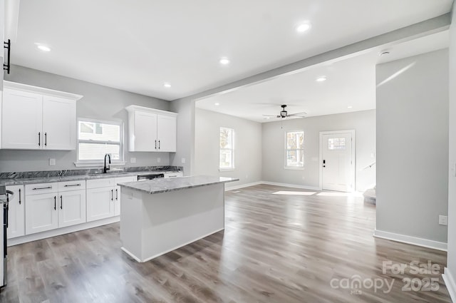 kitchen featuring white cabinetry, light stone counters, a kitchen island, ceiling fan, and a barn door