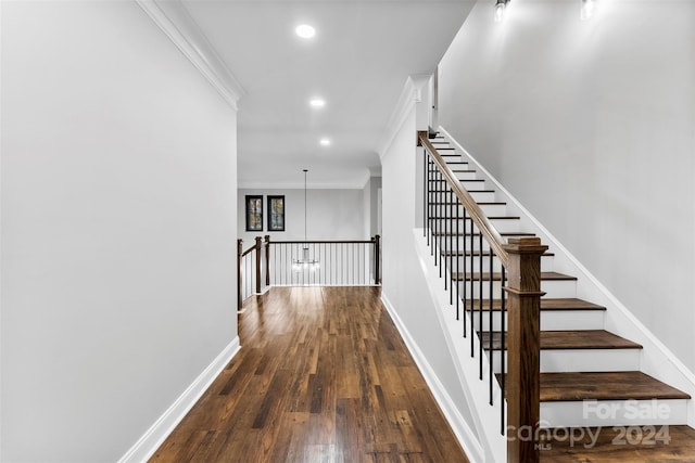 stairs with wood-type flooring, ornamental molding, and an inviting chandelier