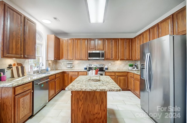 kitchen with a center island, backsplash, sink, light stone counters, and stainless steel appliances