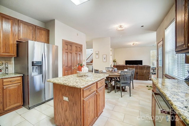 kitchen with backsplash, light stone counters, light tile patterned floors, stainless steel fridge with ice dispenser, and a center island