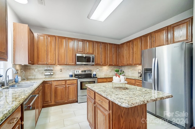 kitchen featuring backsplash, light stone counters, stainless steel appliances, sink, and a center island