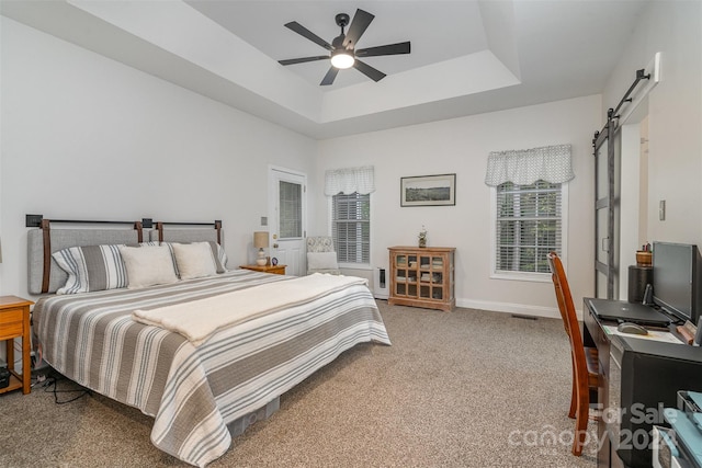 bedroom with a barn door, carpet flooring, ceiling fan, and a raised ceiling