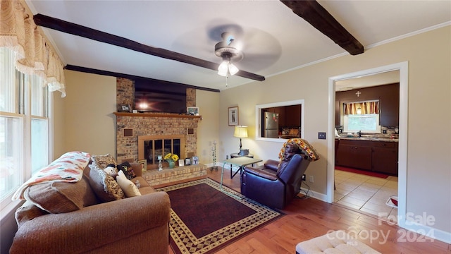 living room featuring beam ceiling, light hardwood / wood-style floors, a brick fireplace, and crown molding