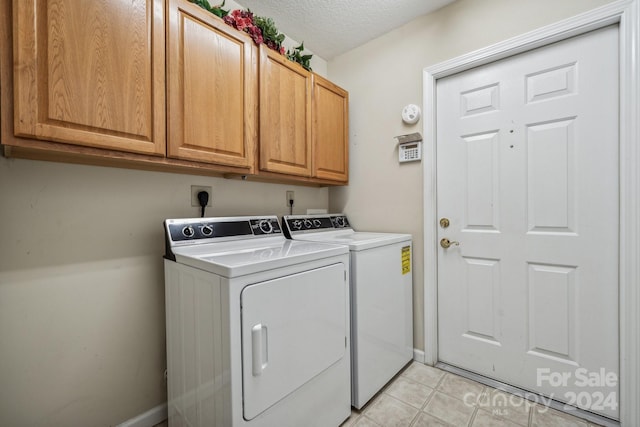 washroom with a textured ceiling, light tile patterned floors, cabinets, and washing machine and clothes dryer