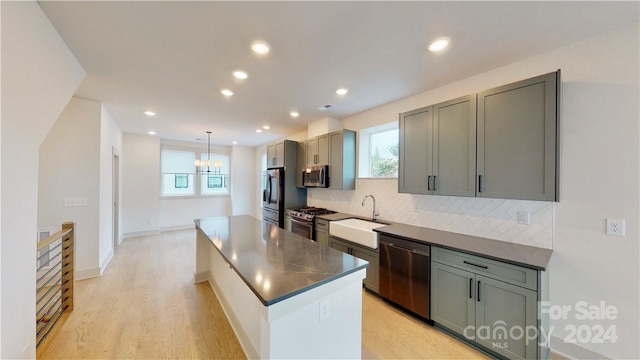 kitchen featuring sink, appliances with stainless steel finishes, hanging light fixtures, light wood-type flooring, and decorative backsplash