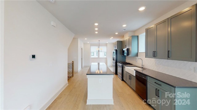 kitchen with gray cabinetry, light wood-type flooring, appliances with stainless steel finishes, decorative light fixtures, and sink