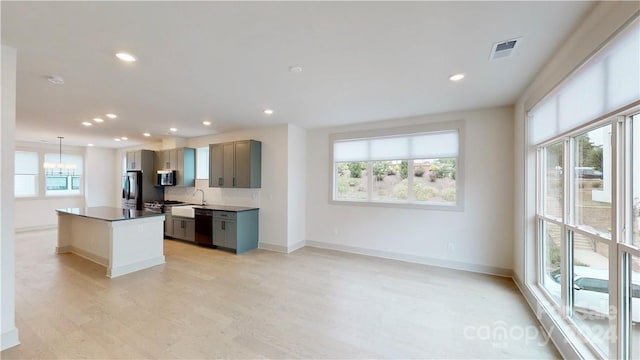 kitchen with gray cabinetry, stainless steel appliances, a kitchen island, pendant lighting, and decorative backsplash