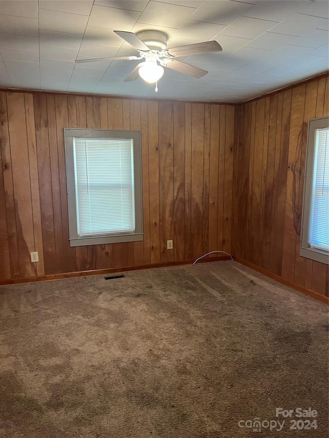 carpeted empty room featuring wood walls and ceiling fan