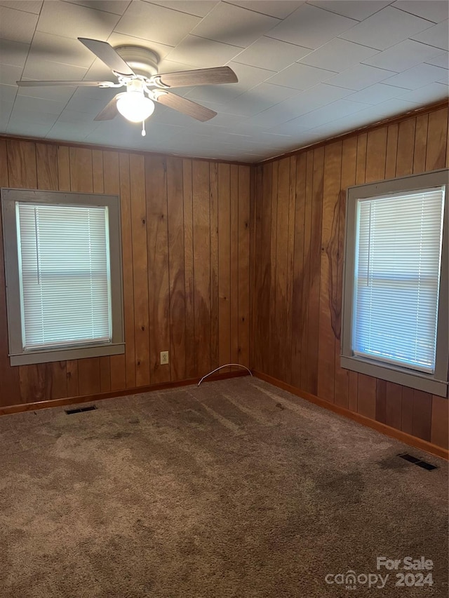 carpeted spare room featuring wooden walls, ceiling fan, and a healthy amount of sunlight