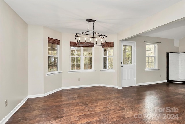 unfurnished dining area with an inviting chandelier, a healthy amount of sunlight, and dark hardwood / wood-style floors