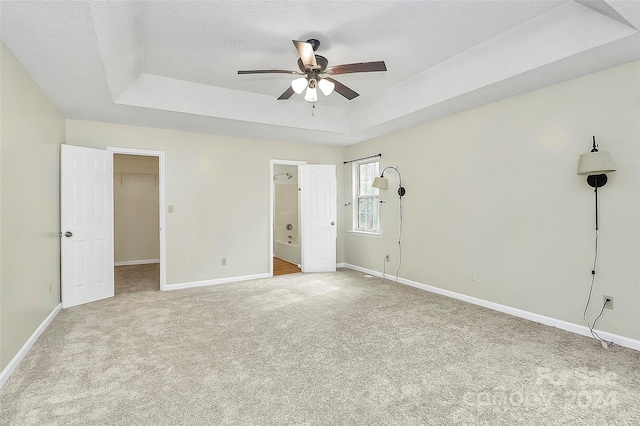 unfurnished bedroom with a tray ceiling, a spacious closet, light carpet, and ceiling fan