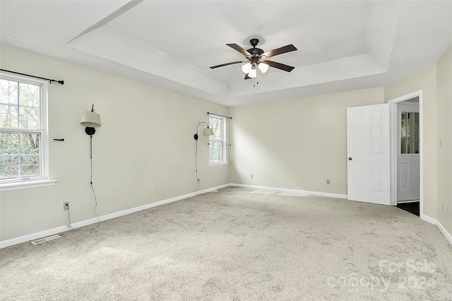 empty room featuring a tray ceiling, ceiling fan, and carpet floors