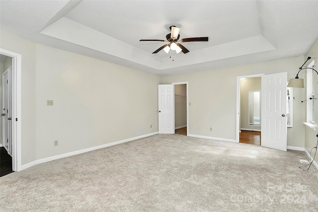 unfurnished bedroom featuring a textured ceiling, carpet, ceiling fan, a tray ceiling, and a spacious closet