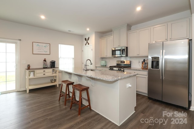 kitchen with stainless steel appliances, a center island with sink, dark wood-type flooring, and white cabinetry