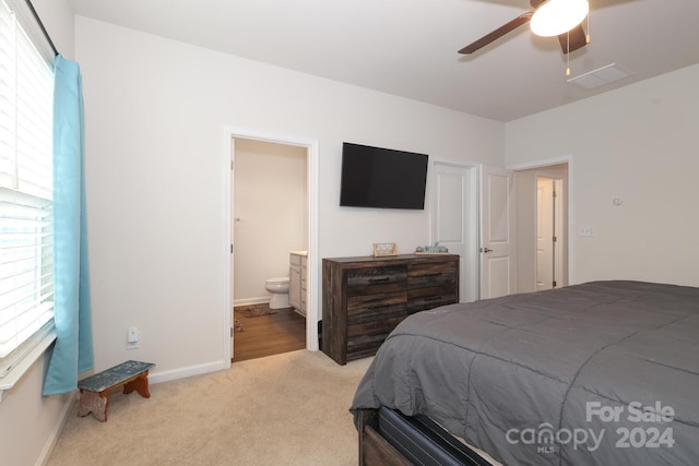 bedroom with ensuite bathroom, ceiling fan, multiple windows, and light colored carpet