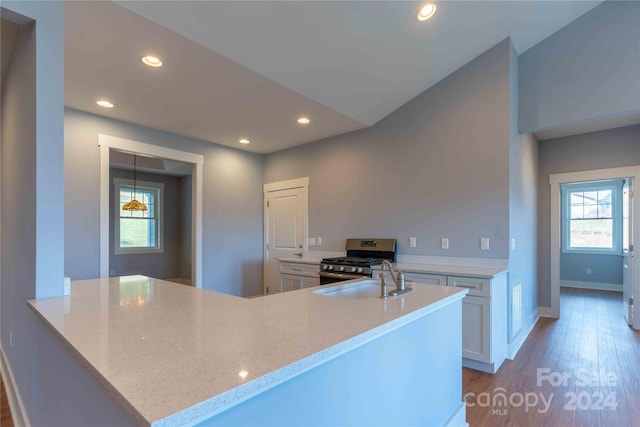 kitchen featuring stainless steel range with gas cooktop, white cabinetry, kitchen peninsula, light stone counters, and wood-type flooring