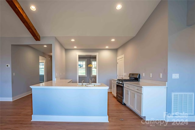 kitchen with light hardwood / wood-style floors, a kitchen island with sink, beam ceiling, stainless steel gas range, and white cabinetry