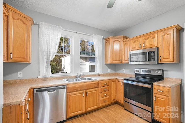 kitchen featuring a textured ceiling, light wood-type flooring, appliances with stainless steel finishes, and sink