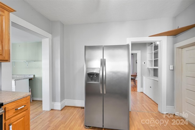 kitchen with light wood-type flooring, stainless steel fridge with ice dispenser, and a textured ceiling