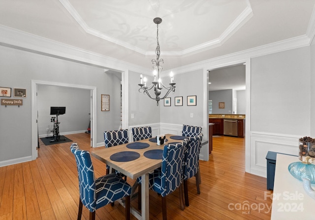 dining area featuring crown molding, light wood-type flooring, a tray ceiling, and an inviting chandelier