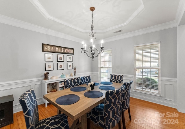 dining area with crown molding, light wood-type flooring, and an inviting chandelier