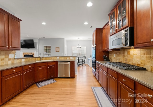 kitchen with sink, pendant lighting, appliances with stainless steel finishes, light hardwood / wood-style floors, and backsplash